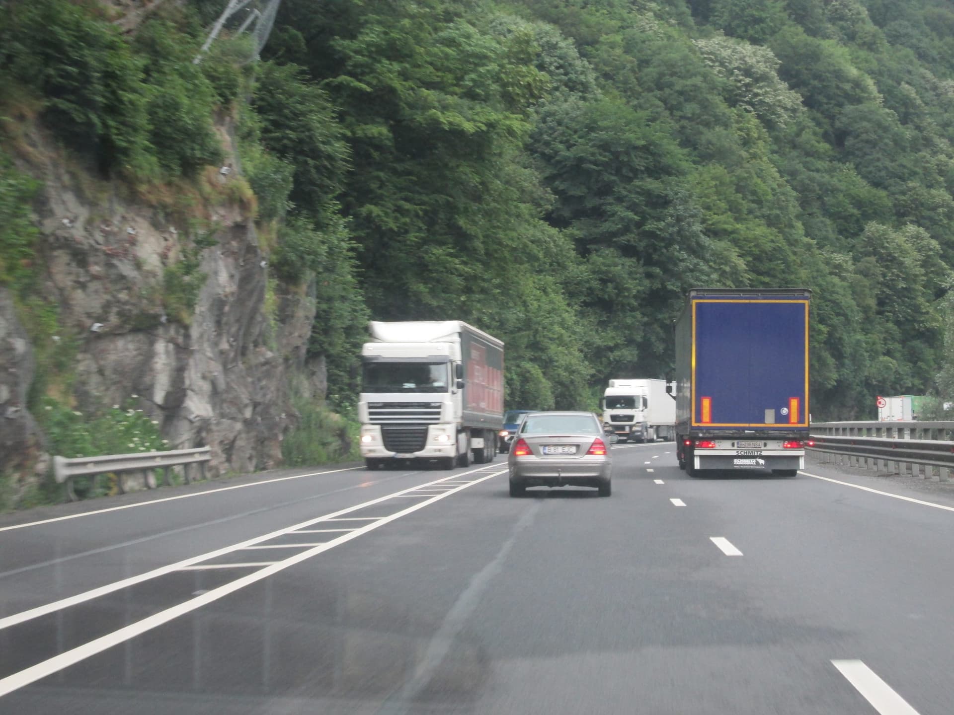 Sectorul de drum cu trei benzi (2+1) al DN 7 pe Valea Oltului, mărginit de versanți împăduriți, cu marcaje rutiere proaspete.