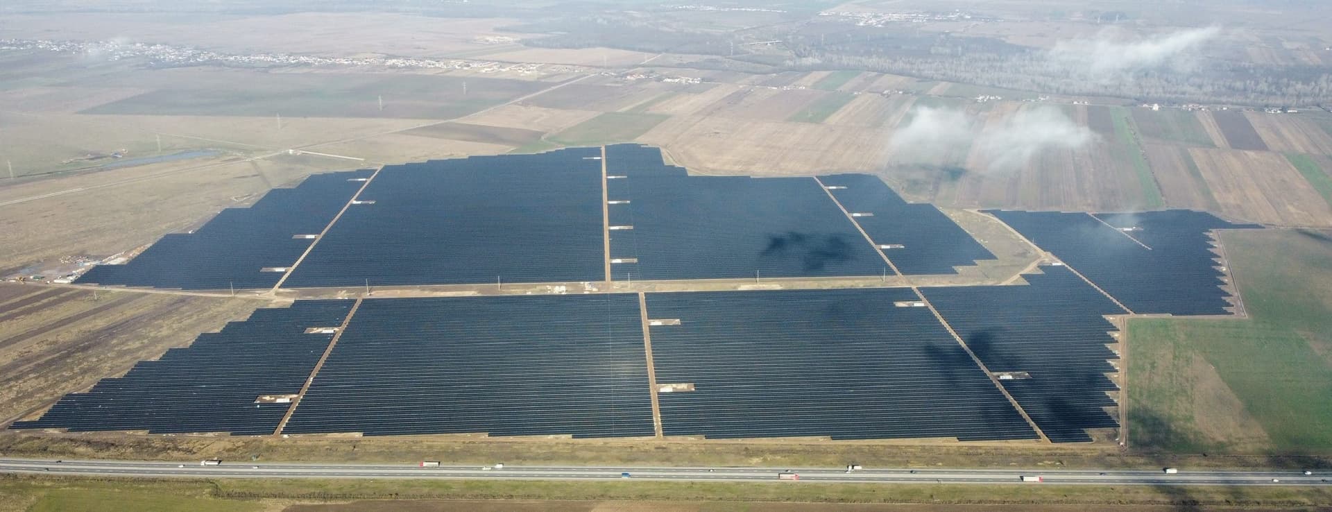 Vedere aeriană a unui parc fotovoltaic din România: rânduri lungi de panouri solare albastre aliniate pe un teren plat